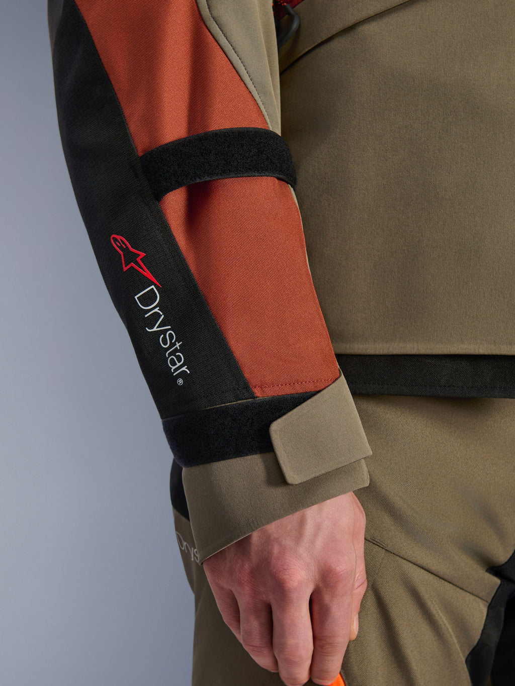 Giacca Alpinestars Andes V4 Drystar®, giacca da moto, Walnut Rust Black, vista ravvicinata della manica con branding Drystar® e logo a stella rosso, cinturini in velcro regolabili su avambraccio e polso, tessuto resistente per touring d'avventura