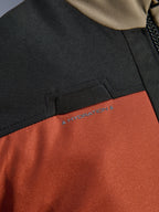 Dettaglio ravvicinato della giacca Alpinestars Andes V4 Drystar® in Walnut Rust Black, che mette in risalto il passante integrato per il tubo di idratazione sul petto e la robusta costruzione in tessuto ripstop.