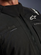 Giacca Alpinestars Andes V4 Drystar®, nera, primo piano del dettaglio del petto con passante per il tubo di idratazione, cerniera anteriore VISLON® impermeabile e logo Alpinestars su materiale tessile resistente