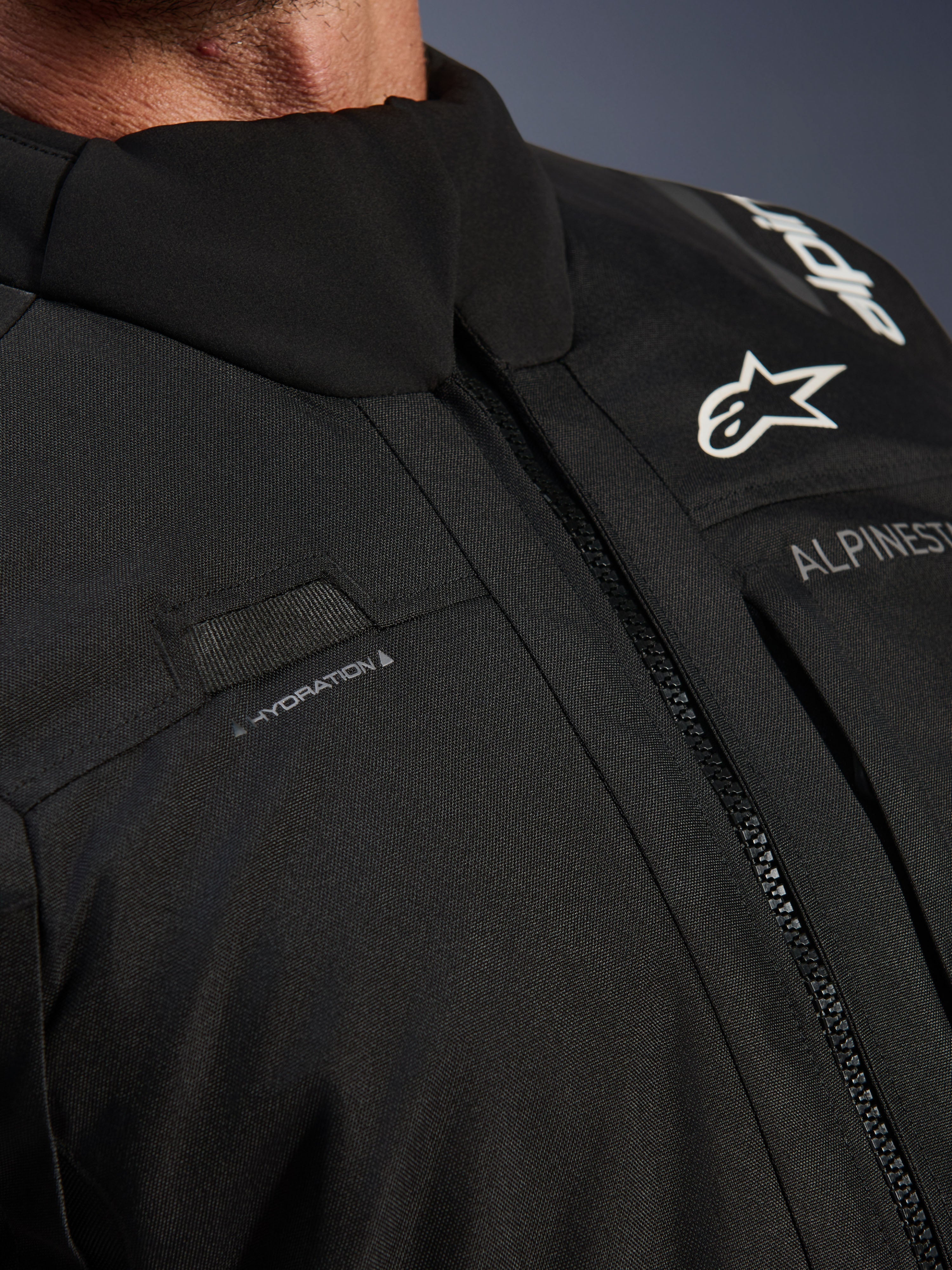 Giacca Alpinestars Andes V4 Drystar®, nera, primo piano del dettaglio del petto con passante per il tubo di idratazione, cerniera anteriore VISLON® impermeabile e logo Alpinestars su materiale tessile resistente