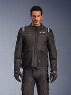 Modello maschile con giacca Alpinestars Andes V4 Drystar® nera, giacca da moto adventure touring, abbinata a pantaloni e guanti neri coordinati, con cerniere impermeabili e logo Alpinestars bianco su petto e spalle, scatto in studio per abbigliamento tecnico da moto per ogni condizione atmosferica.
