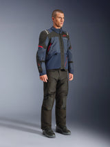 Modello che indossa la giacca Alpinestars Andes V4 Drystar® nei colori Night Navy e Mood Indigo con pannelli neri e dettagli rossi, abbinata a pantaloni e stivali da moto neri, abbigliamento tecnico da adventure touring in un ambiente da studio.