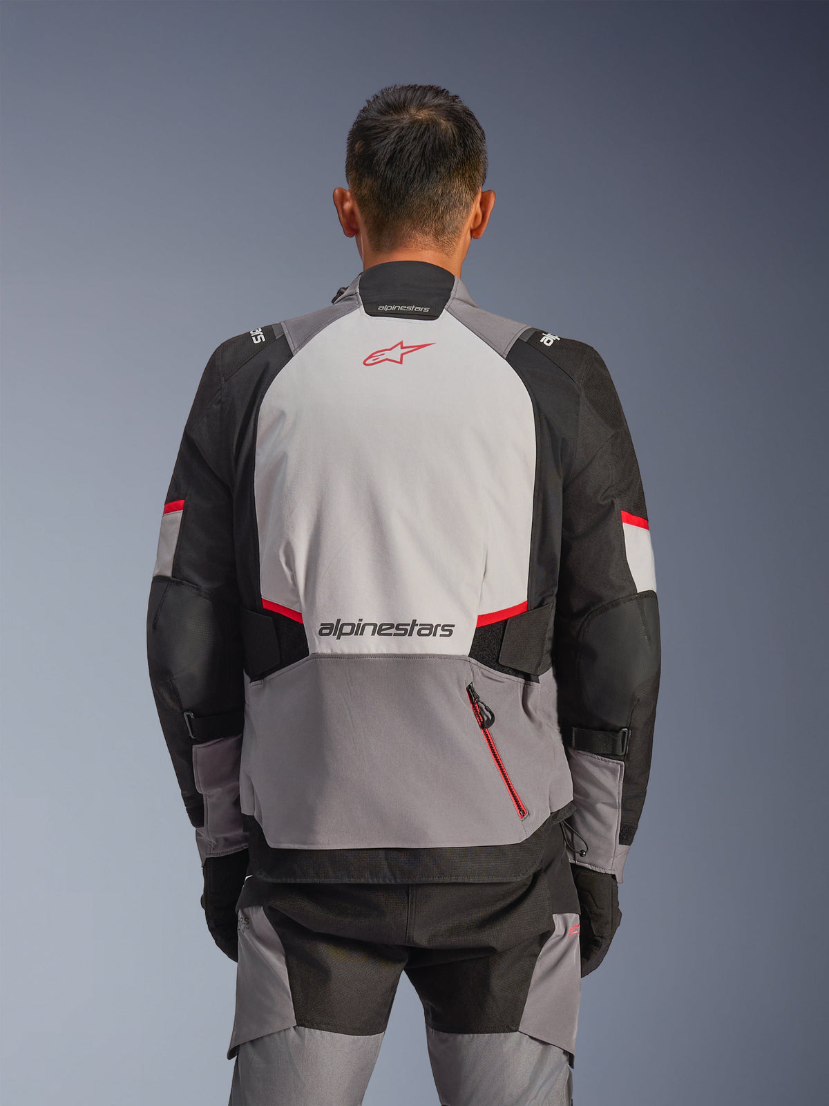 Giacca Alpinestars Andes V4 Drystar®, vista posteriore, grigio scuro, grigio ghiaccio, nero e rosso brillante, con logo Astar rosso e scritta Alpinestars sul retro, pannelli rinforzati e una tasca con zip rossa, abbigliamento da moto adventure