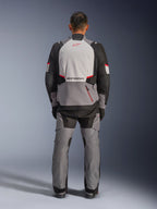 Giacca Alpinestars Andes V4 Drystar®, giacca da moto adventure, grigio scuro, grigio ghiaccio, nero e rosso brillante, vista posteriore di un pilota che indossa pantaloni coordinati, con un ampio pannello posteriore grigio ghiaccio e logo rosso, sezioni rinforzate sulle spalle nere e cinghie regolabili in vita per il touring in ogni condizione atmosferica.