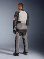 Giacca Alpinestars Andes V4 Drystar®, grigio scuro e grigio ghiaccio con accenti nero e rosso brillante, vista posteriore che mostra il pannello grigio chiaro con logo della stella rossa, abbinata a pantaloni adventure coordinati e guanti neri, abbigliamento tecnico da moto per ogni condizione atmosferica.
