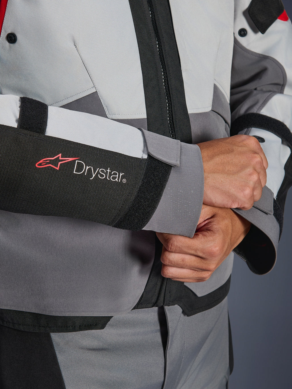 Dettaglio ravvicinato della manica della giacca Alpinestars Andes V4 Drystar®, tessuto grigio e nero, con logo Drystar rosso e bianco sull'avambraccio, chiusura del polso regolabile in velcro, abbigliamento da moto impermeabile ad alte prestazioni