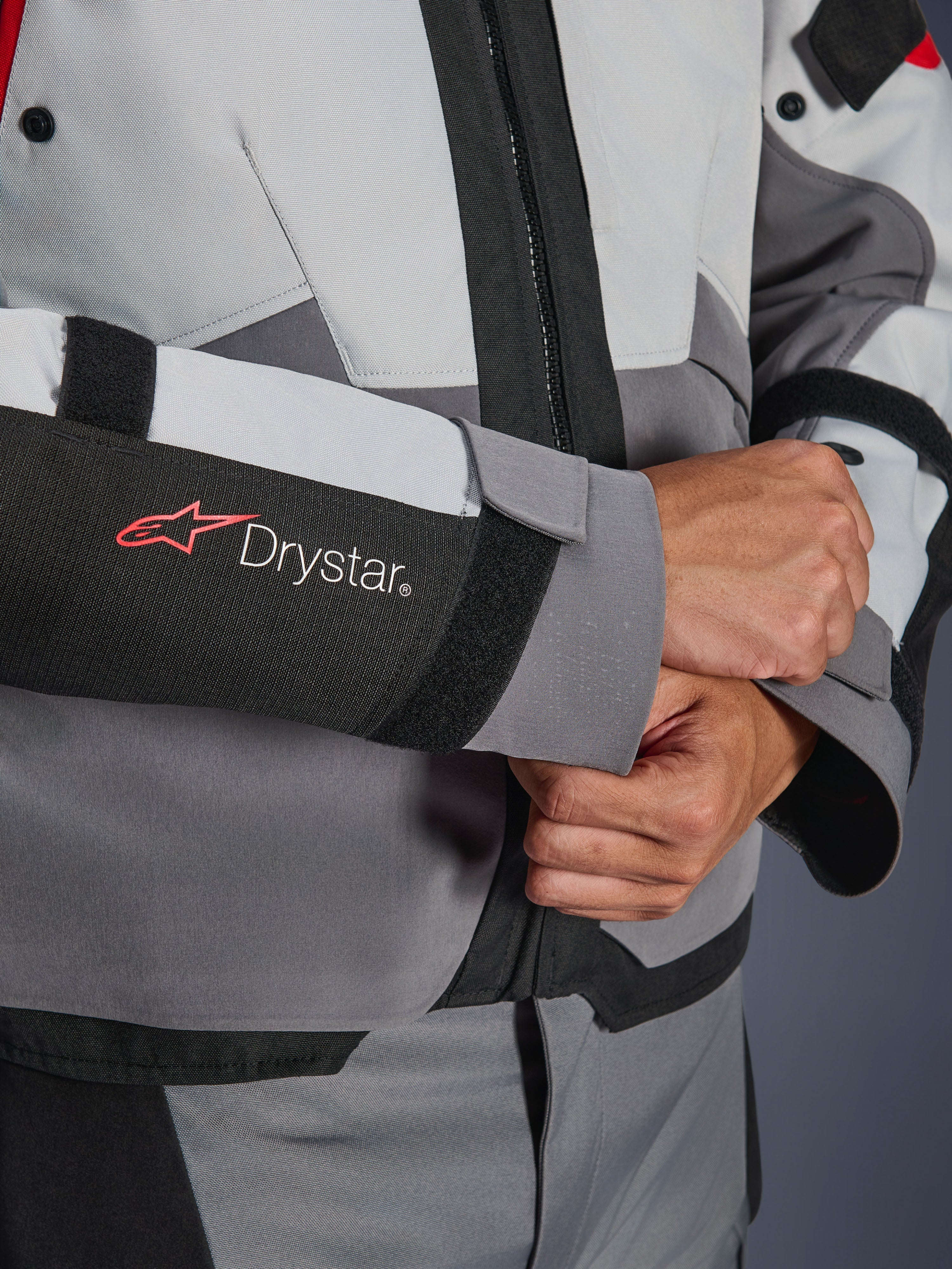 Dettaglio ravvicinato della manica della giacca Alpinestars Andes V4 Drystar®, tessuto grigio e nero, con logo Drystar rosso e bianco sull'avambraccio, chiusura del polso regolabile in velcro, abbigliamento da moto impermeabile ad alte prestazioni