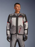 Giacca Alpinestars Andes V4 Drystar®, giacca da moto adventure touring, grigio scuro e grigio ghiaccio con dettagli neri e rosso acceso, indossata con pantaloni e guanti abbinati, design impermeabile e traspirante per la guida adventure in ogni condizione climatica