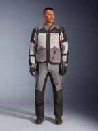 Giacca Alpinestars Andes V4 Drystar®, giacca da moto adventure, grigio scuro, grigio ghiaccio, nero e rosso acceso, indossata con pantaloni in tessuto e guanti coordinati, caratterizzata da un design tecnico multi-pannello con logo Alpinestars rosso, abbigliamento adventure-touring.