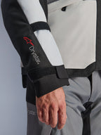 Alpinestars Andes V4 Drystar® Jacket, giacca da moto adventure, pannelli grigio ghiaccio e neri, primo piano della manica con logo Drystar® rosso e cinghie regolabili, design in tessuto funzionale per la guida con ogni condizione atmosferica
