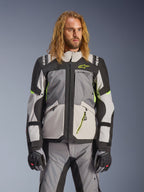 Giacca Alpinestars Andes V4 Drystar, giacca da moto adventure touring, grigio scuro e grigio ghiaccio con dettagli giallo neon, indossata da un modello con pantaloni e guanti coordinati, design multitasca in tessuto per la guida in ogni condizione atmosferica