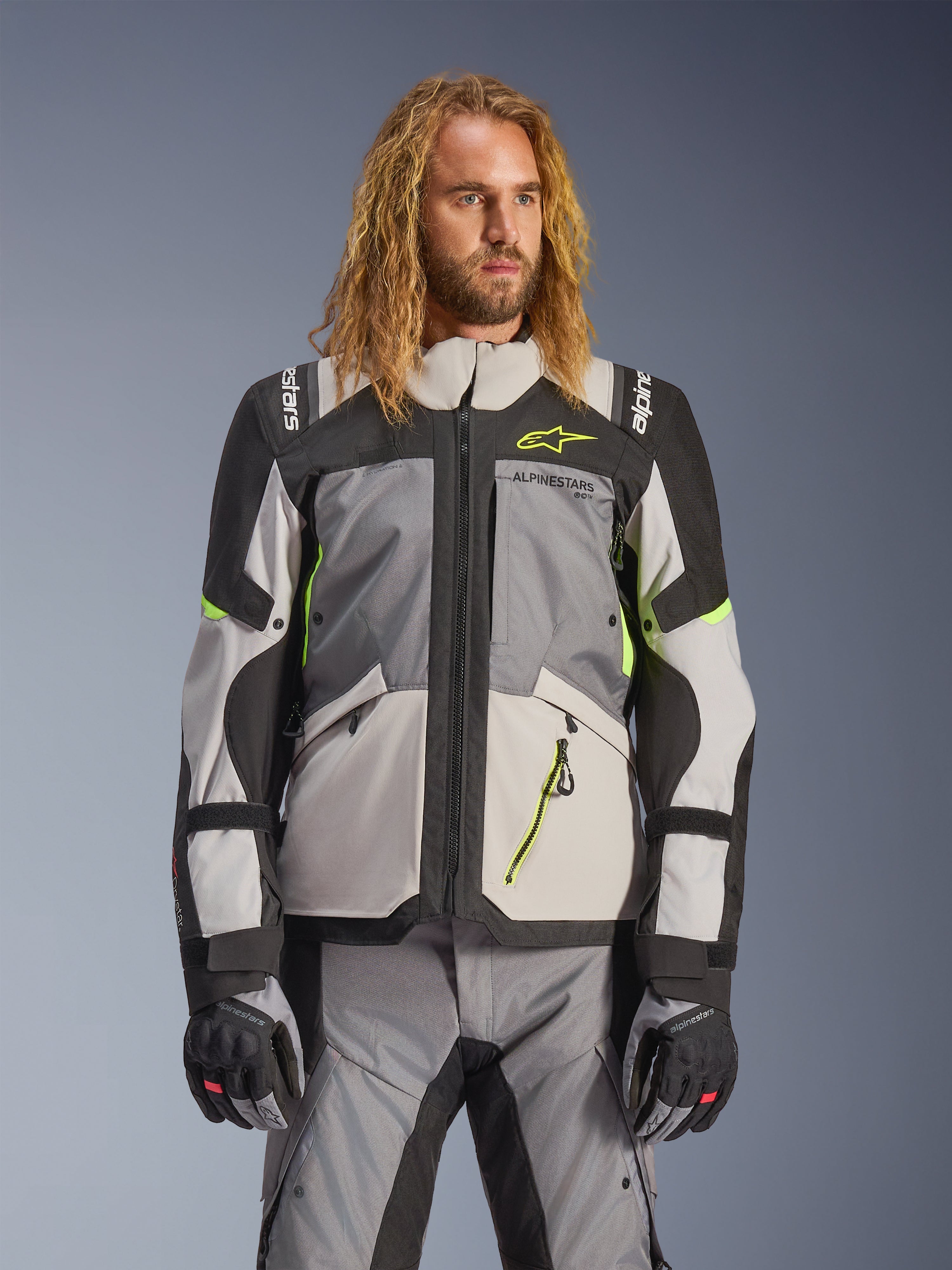 Giacca Alpinestars Andes V4 Drystar, giacca da moto adventure touring, grigio scuro e grigio ghiaccio con dettagli giallo neon, indossata da un modello con pantaloni e guanti coordinati, design multitasca in tessuto per la guida in ogni condizione atmosferica