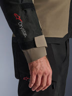 Dettaglio della giacca Alpinestars Andes V4 Drystar® in Walnut e Black, con logo Drystar® rosso sull'avambraccio e cinturino regolabile sul polsino, parte di un completo tecnico da moto adventure.