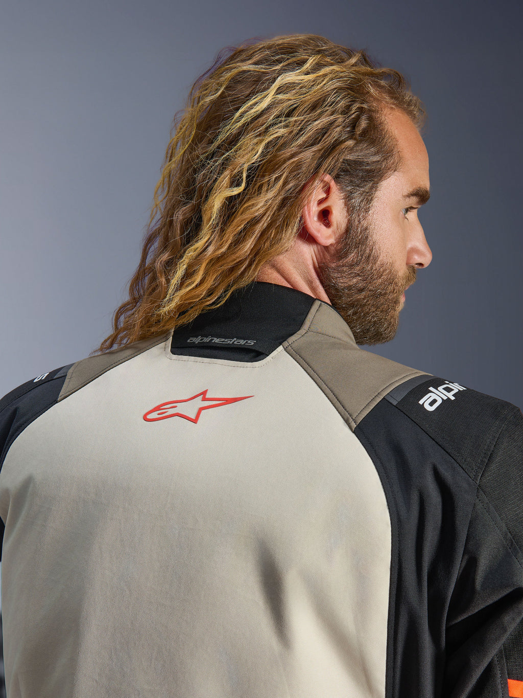 Giacca Alpinestars Andes V4 Drystar®, colorazione Walnut Mastic Black, vista ravvicinata della parte superiore della schiena e del colletto, con logo a stella rosso sul pannello mastice, struttura in tessuto walnut e nero, abbigliamento per mototurismo d'avventura