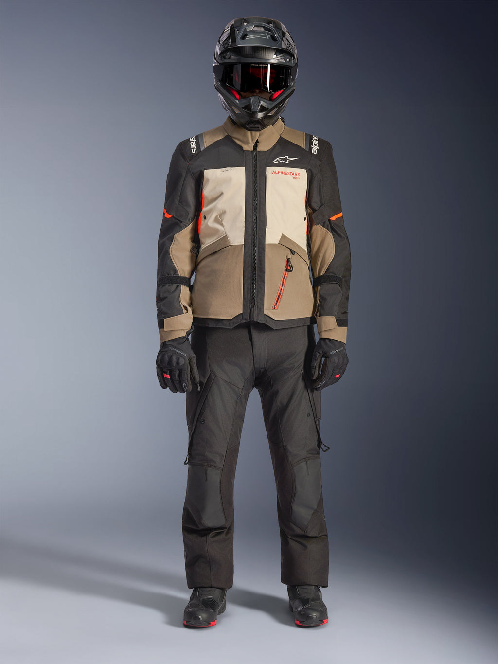 Alpinestars Andes V4 Drystar® Jacket, Walnut Mastic Black, giacca da moto adventure touring con pannelli sabbia e panna e dettagli arancioni, indossata da un pilota con casco adventure nero, pantaloni da moto neri e stivali neri, vista a figura intera in studio