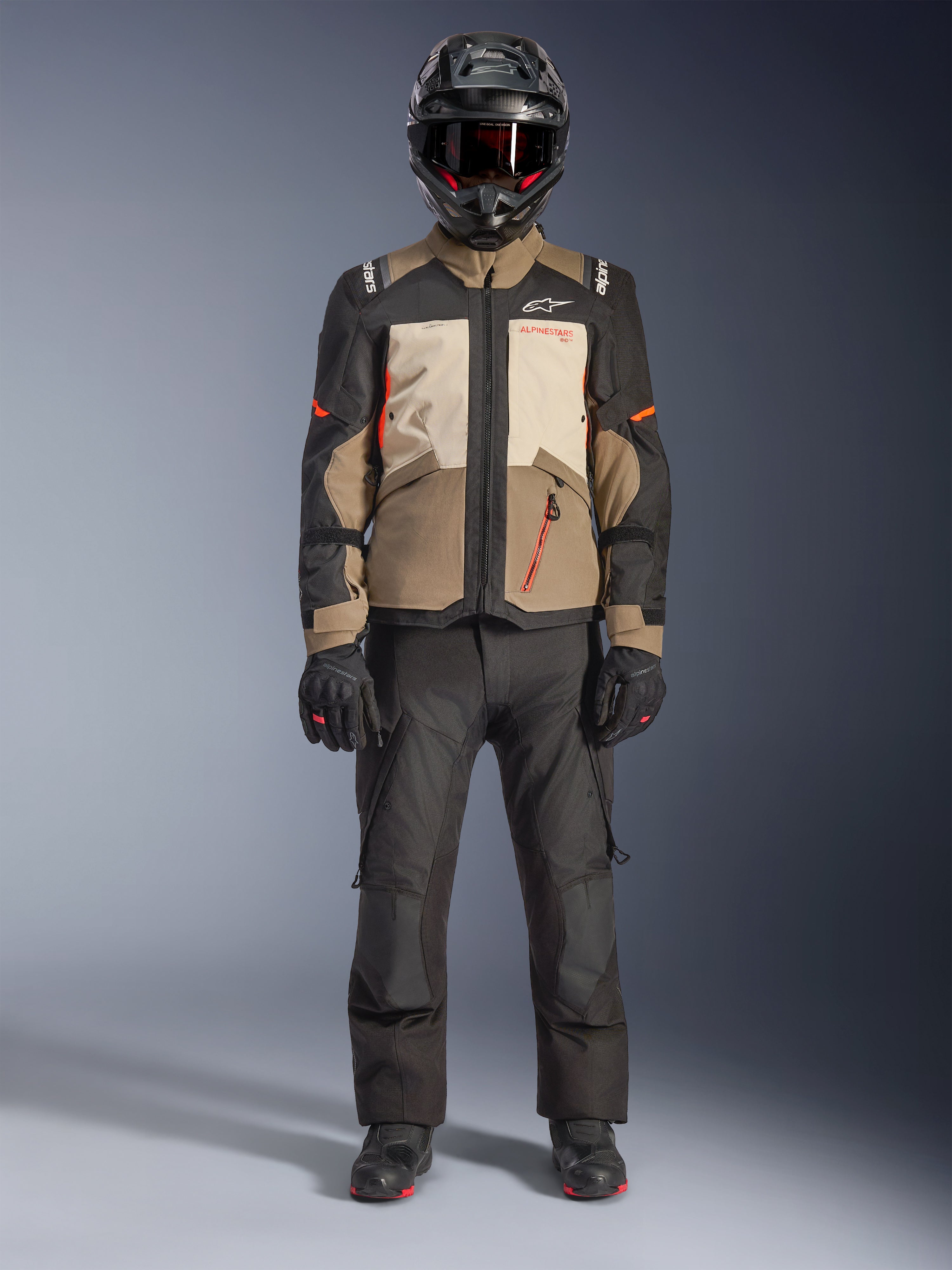 Alpinestars Andes V4 Drystar® Jacket, Walnut Mastic Black, giacca da moto adventure touring con pannelli sabbia e panna e dettagli arancioni, indossata da un pilota con casco adventure nero, pantaloni da moto neri e stivali neri, vista a figura intera in studio
