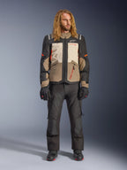Giacca Alpinestars Andes V4 Drystar®, Walnut Mastic Black, indossata con pantaloni e guanti da moto neri, design adventure multi-pannello con accenti arancioni e marchio Alpinestars, abbigliamento tecnico in tessuto per ogni condizione atmosferica