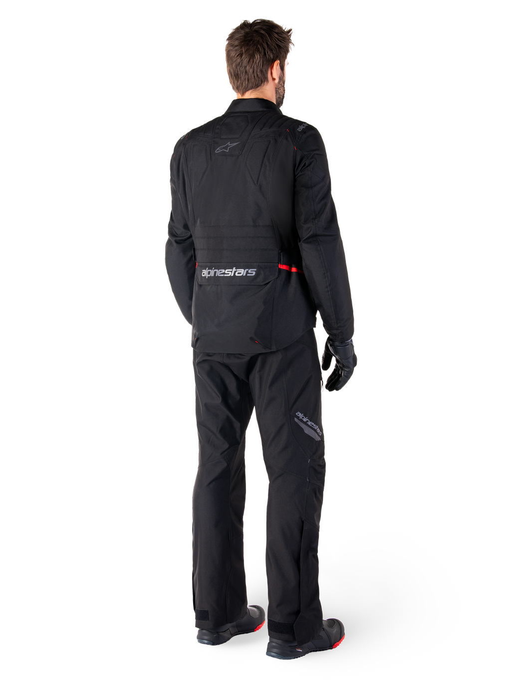Rear view of a rider wearing the Alpinestars ST-1 Waterproof Jacket and matching pants in black, featuring subtle red accents, a large lower back cargo pocket with branding, and a streamlined adventure touring design.