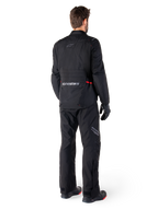 Rear view of a rider wearing the Alpinestars ST-1 Waterproof Jacket and matching pants in black, featuring subtle red accents, a large lower back cargo pocket with branding, and a streamlined adventure touring design.