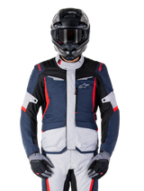 Giacca Alpinestars ST-1 Waterproof, giacca da adventure touring, blu scuro, nero e rosso brillante, indossata con casco adventure nero e guanti grigi, pannelli grigio chiaro e accenti rossi su spalle e cerniere, design elegante con logo Alpinestars sul petto, abbigliamento impermeabile resistente per la guida in moto