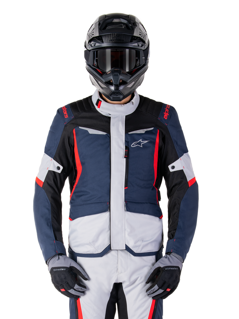 Giacca Alpinestars ST-1 Waterproof, giacca da adventure touring, blu scuro, nero e rosso brillante, indossata con casco adventure nero e guanti grigi, pannelli grigio chiaro e accenti rossi su spalle e cerniere, design elegante con logo Alpinestars sul petto, abbigliamento impermeabile resistente per la guida in moto