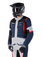 Giacca Alpinestars ST-1 Waterproof, giacca da moto adventure touring in blu scuro, nero e rosso acceso, indossata con un casco nero e guanti grigi, caratterizzata da un design moderno con tasche funzionali e marchio Alpinestars.