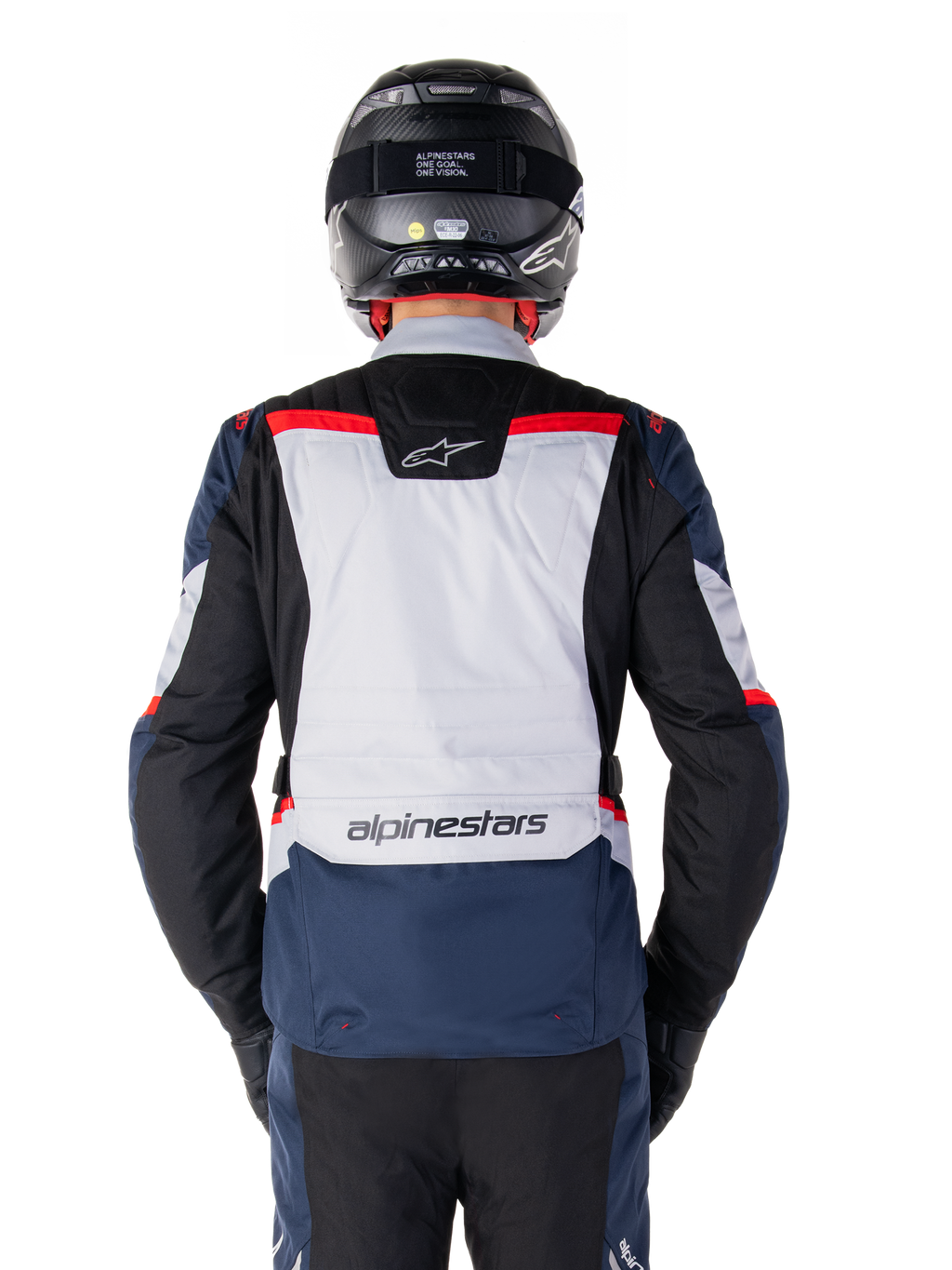 Giacca impermeabile Alpinestars ST-1, blu scuro, nero e rosso acceso, vista posteriore con pannello grigio chiaro e logo, giacca da moto adventure touring indossata con casco e guanti neri, design aerodinamico per ogni condizione atmosferica