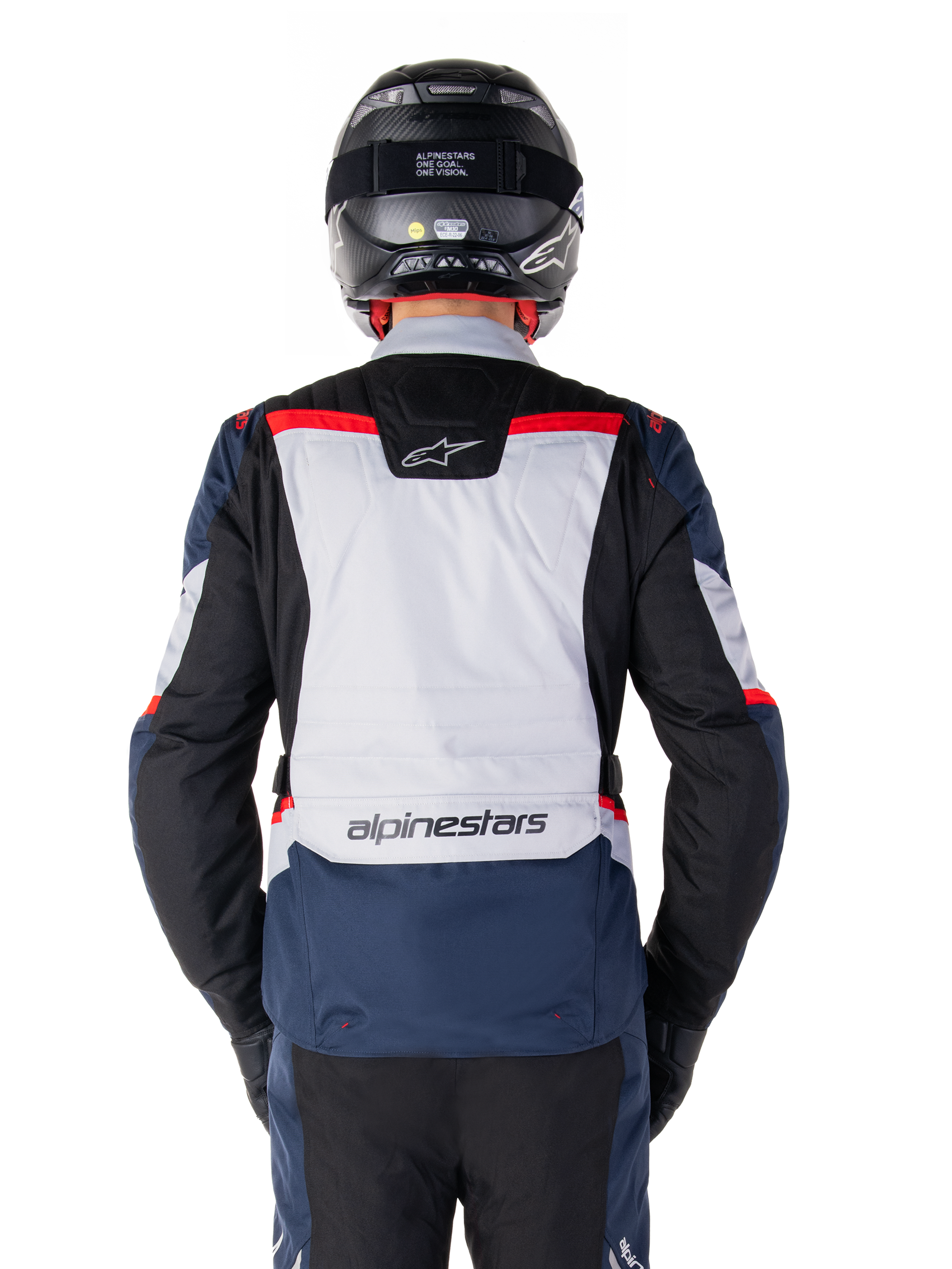 Giacca impermeabile Alpinestars ST-1, blu scuro, nero e rosso acceso, vista posteriore con pannello grigio chiaro e logo, giacca da moto adventure touring indossata con casco e guanti neri, design aerodinamico per ogni condizione atmosferica