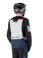 Giacca Alpinestars ST-1 Waterproof, blu scuro, nero e rosso brillante, vista posteriore su un pilota con casco da adventure nero, caratterizzata da pannelli grigio chiaro e logo Alpinestars, abbigliamento da moto adventure touring