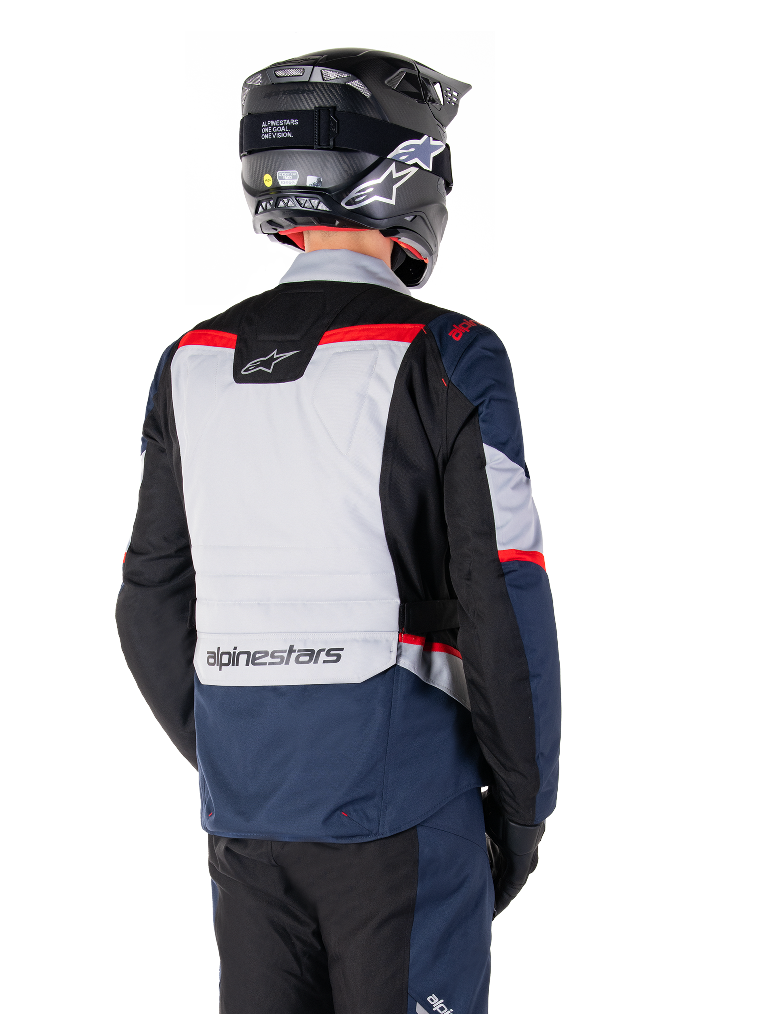 Giacca Alpinestars ST-1 Waterproof, blu scuro, nero e rosso brillante, vista posteriore su un pilota con casco da adventure nero, caratterizzata da pannelli grigio chiaro e logo Alpinestars, abbigliamento da moto adventure touring