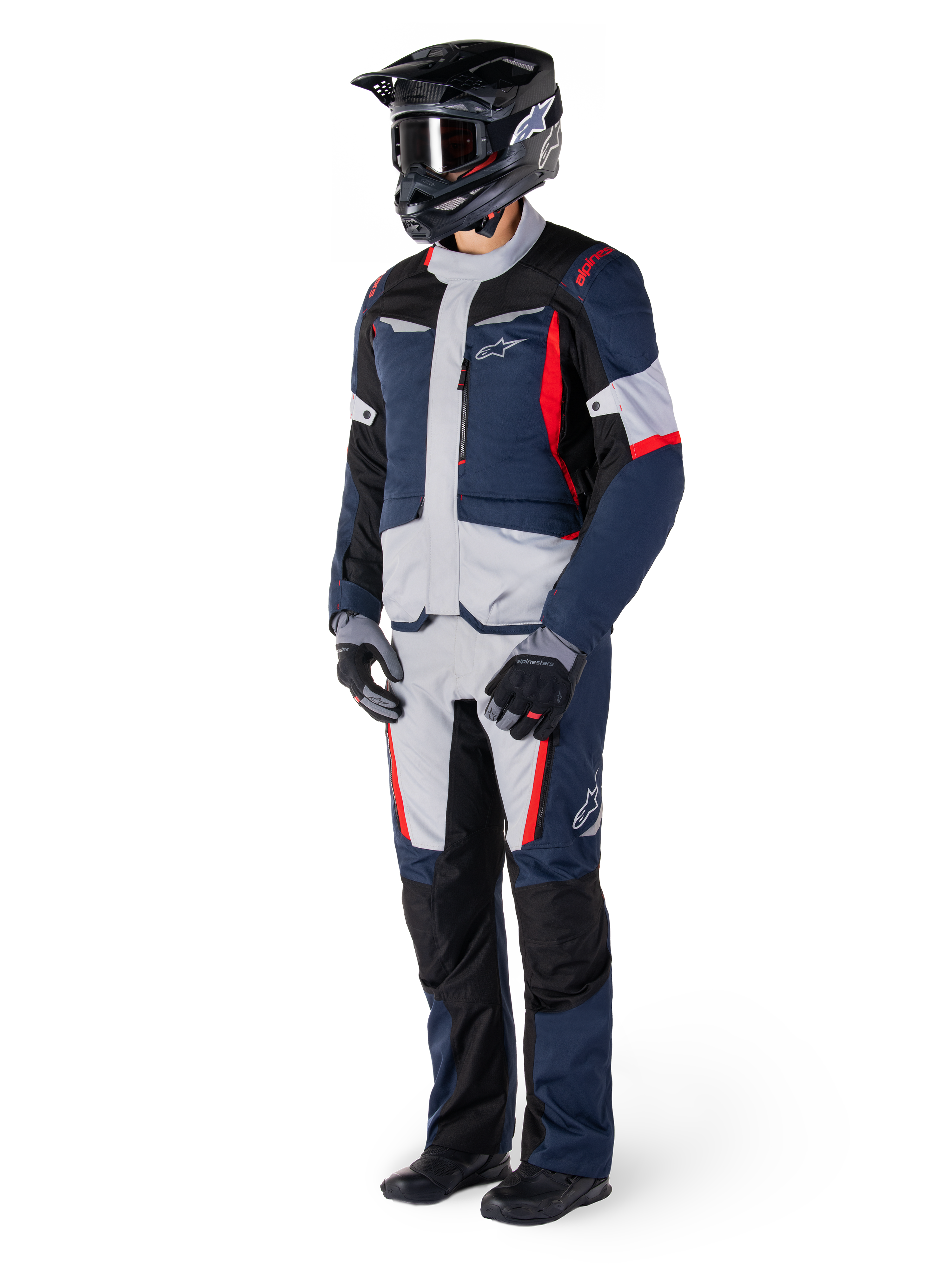 Giacca Impermeabile Alpinestars ST-1, giacca da adventure touring, blu scuro, nero e rosso acceso, indossata da un pilota con pantaloni coordinati, casco da adventure nero, guanti e stivali, con pannelli grigi e accenti rossi, design aerodinamico ispirato all'adventure con loghi Alpinestars