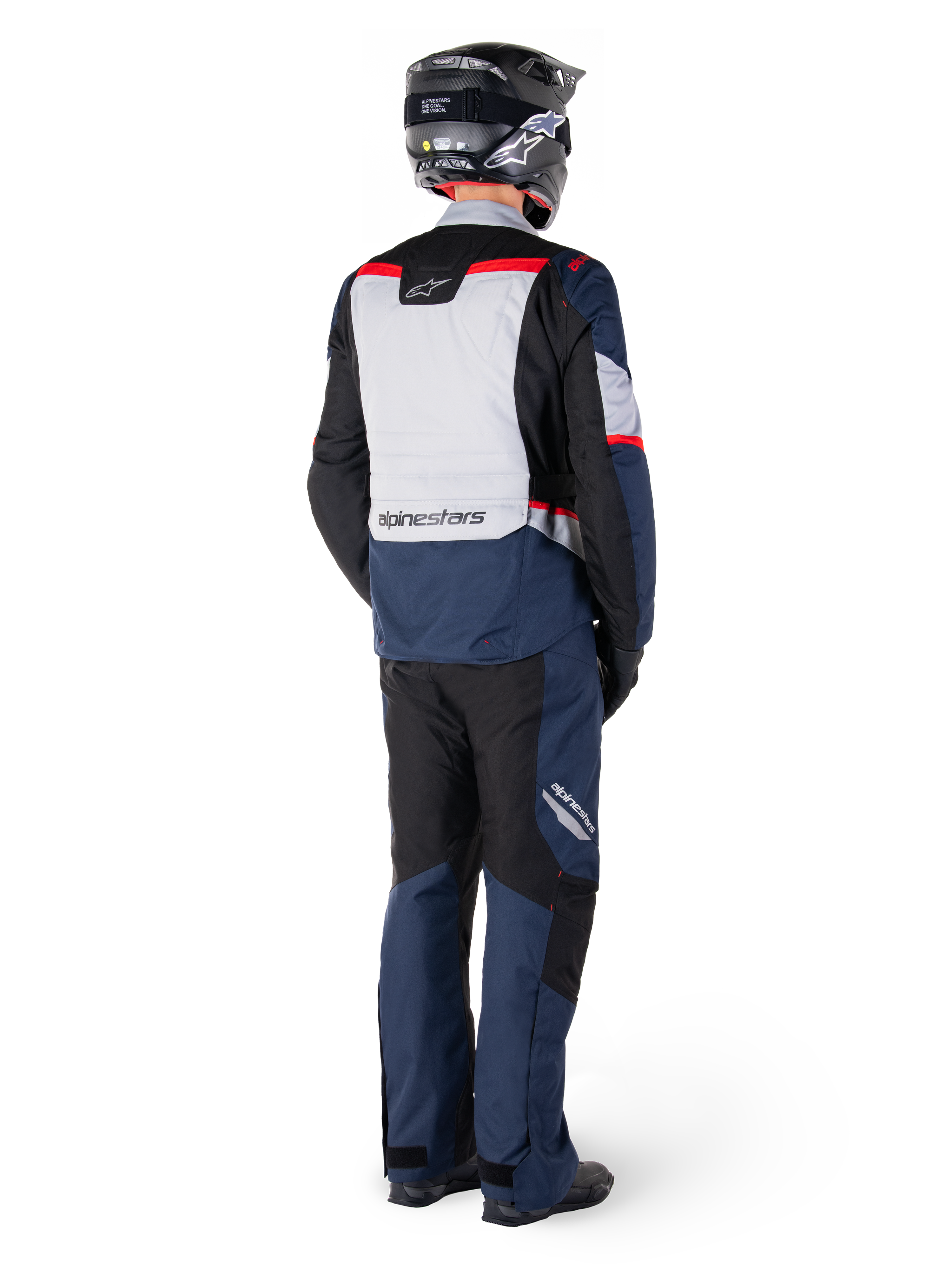 Vista posteriore di un pilota che indossa la giacca Alpinestars ST-1 Waterproof Jacket in Dark Blue Black Bright Red, abbinata a pantaloni impermeabili coordinati e un casco nero, caratterizzata da un pannello posteriore grigio con marchio Alpinestars e un design adventure touring.