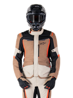 Giacca Alpinestars ST-1 Waterproof, Dark Khaki Sand Black Red Fluo, indossata da un pilota con casco e guanti neri, abbigliamento adventure touring con pannelli beige e marroni e vivaci accenti rosso fluo, vista frontale su sfondo bianco.