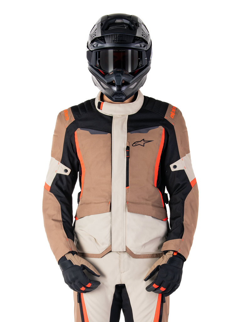 Giacca Alpinestars ST-1 Waterproof, Dark Khaki Sand Black Red Fluo, indossata da un pilota con casco e guanti neri, abbigliamento adventure touring con pannelli beige e marroni e vivaci accenti rosso fluo, vista frontale su sfondo bianco.