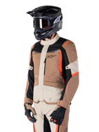 Giacca Alpinestars ST-1 Waterproof, giacca adventure touring, Dark Khaki Sand nero e rosso fluo, indossata da un pilota con casco da motocross nero e occhiali, caratterizzata da un design a pannelli con tasche cargo e branding Alpinestars sul petto