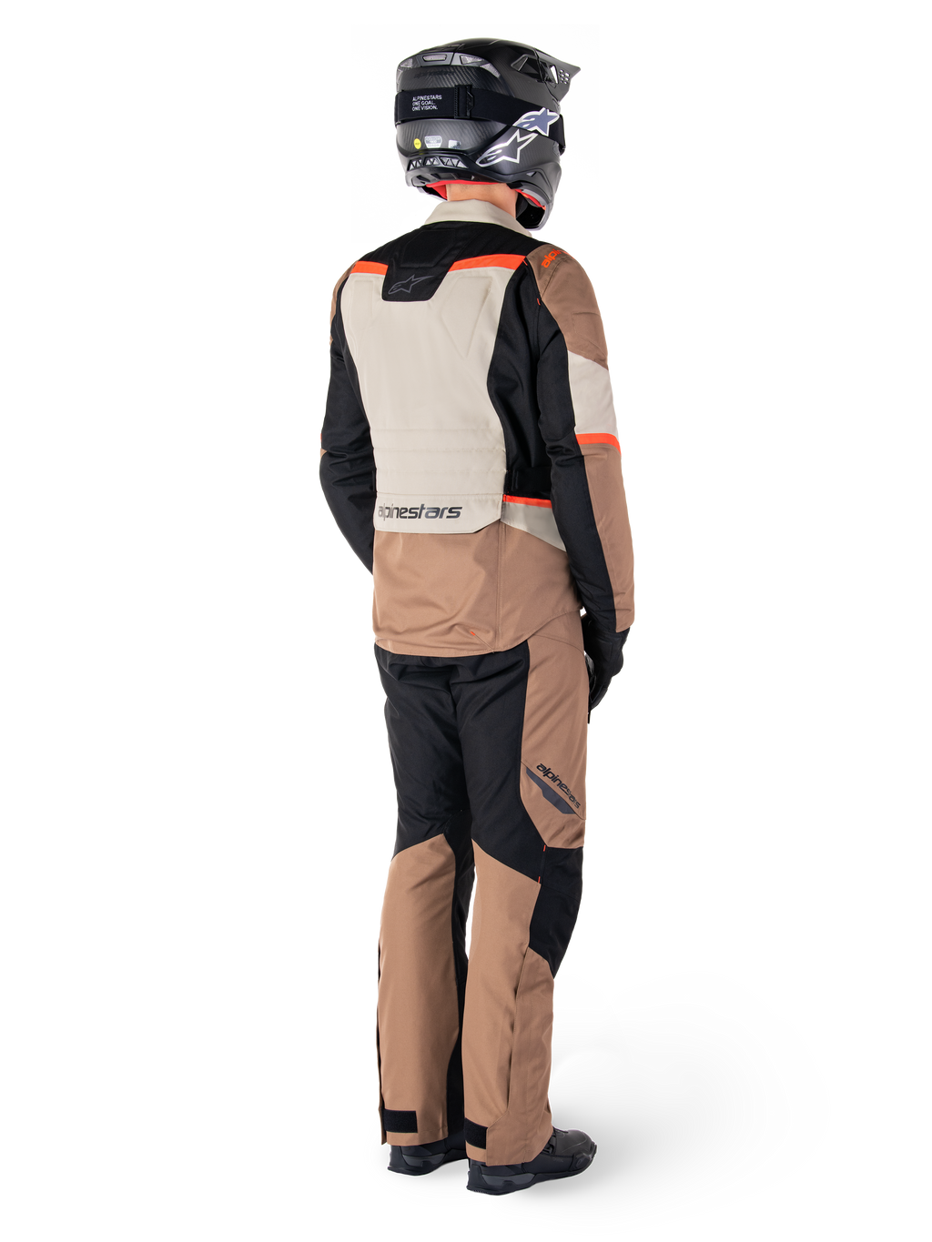 Giacca impermeabile Alpinestars ST-1, giacca da adventure touring, Dark Khaki Sand Black Red Fluo, vista posteriore indossata con pantaloni coordinati e casco nero, caratterizzata da pannelli a blocchi di colore e accenti rosso fluorescente.