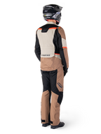 Giacca impermeabile Alpinestars ST-1, giacca da adventure touring, Dark Khaki Sand Black Red Fluo, vista posteriore indossata con pantaloni coordinati e casco nero, caratterizzata da pannelli a blocchi di colore e accenti rosso fluorescente.
