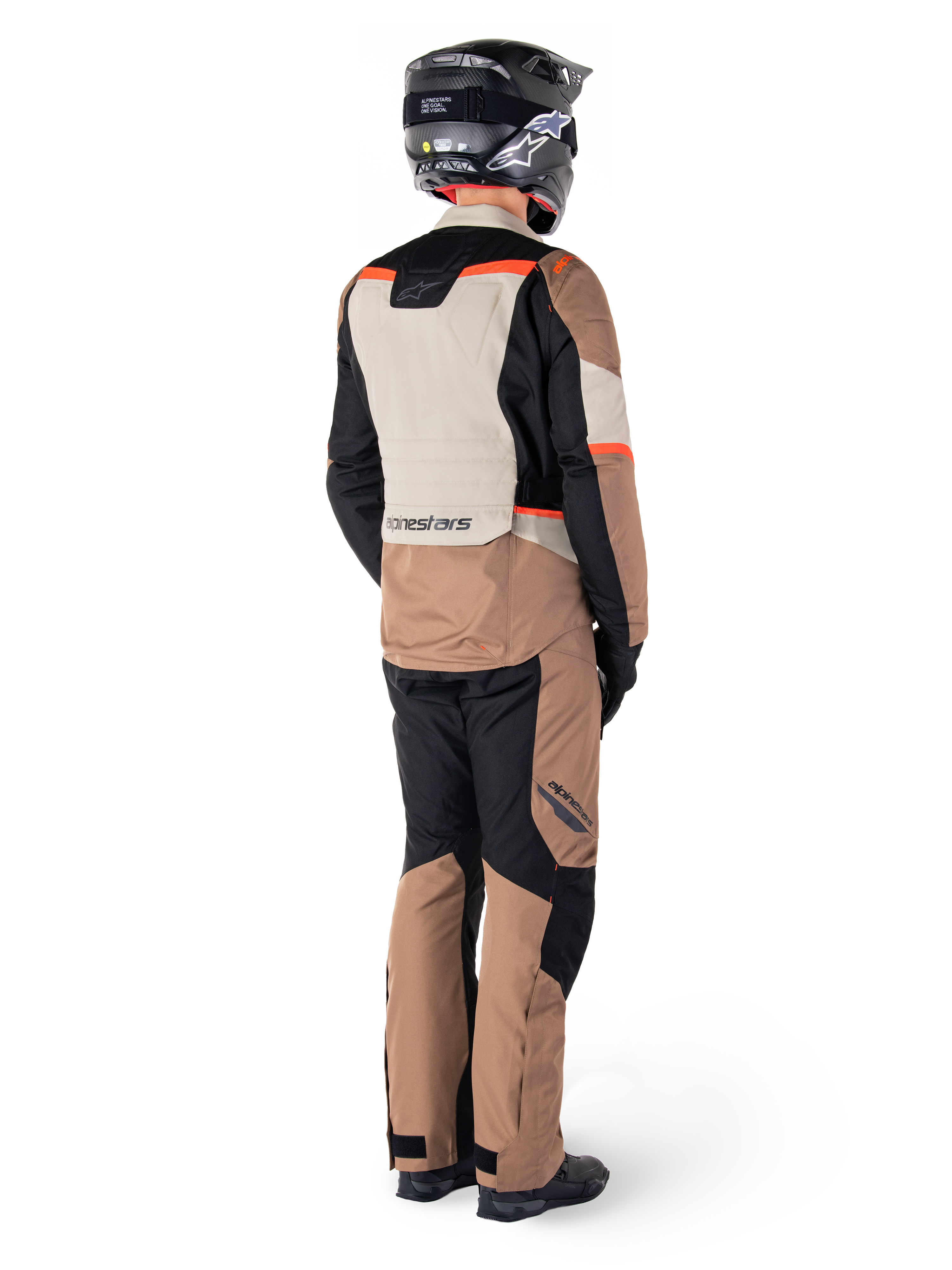 Giacca impermeabile Alpinestars ST-1, giacca da adventure touring, Dark Khaki Sand Black Red Fluo, vista posteriore indossata con pantaloni coordinati e casco nero, caratterizzata da pannelli a blocchi di colore e accenti rosso fluorescente.