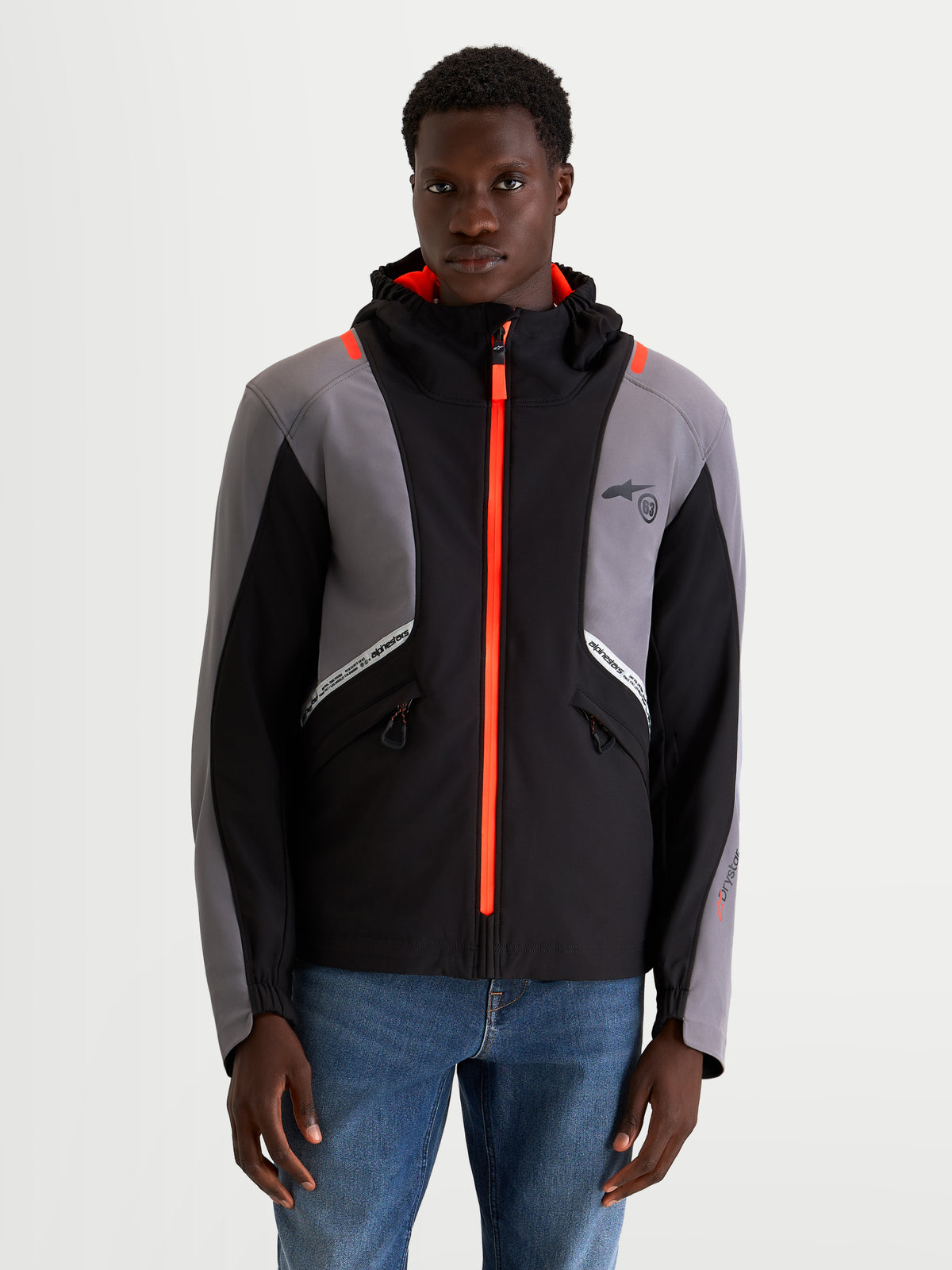 Alpinestars C 5 Drystar Giacca, giacca da moto urbana contemporanea da uomo in nero e grigio scuro, vista frontale su un modello che mostra la struttura softshell impermeabile, il cappuccio integrato e dettagli con cerniera arancione brillante