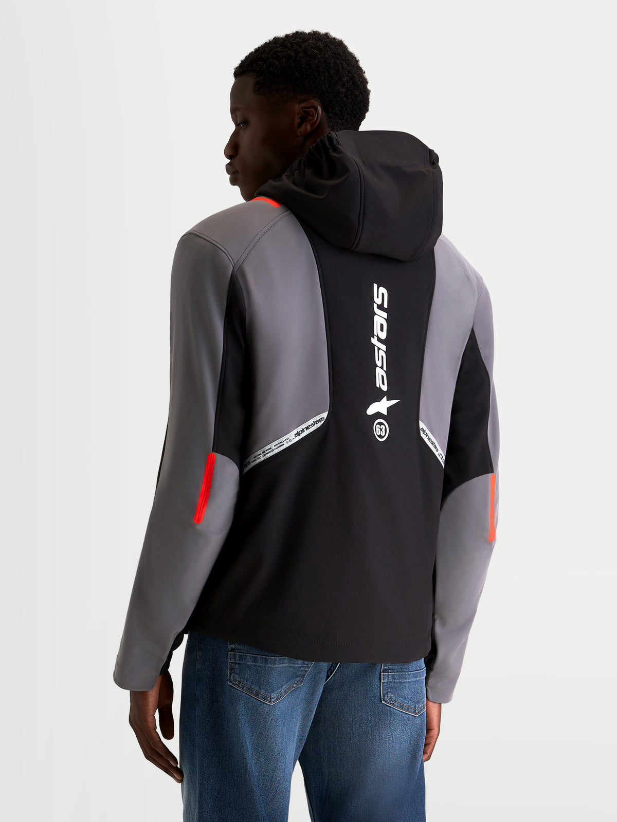 Alpinestars C 5 Drystar Giacca, giacca da moto urban softshell da uomo in nero e grigio scuro, vista posteriore su un modello che mostra il cappuccio integrato, il grande marchio Alpinestars riflettente sul retro e la struttura in tessuto impermeabile