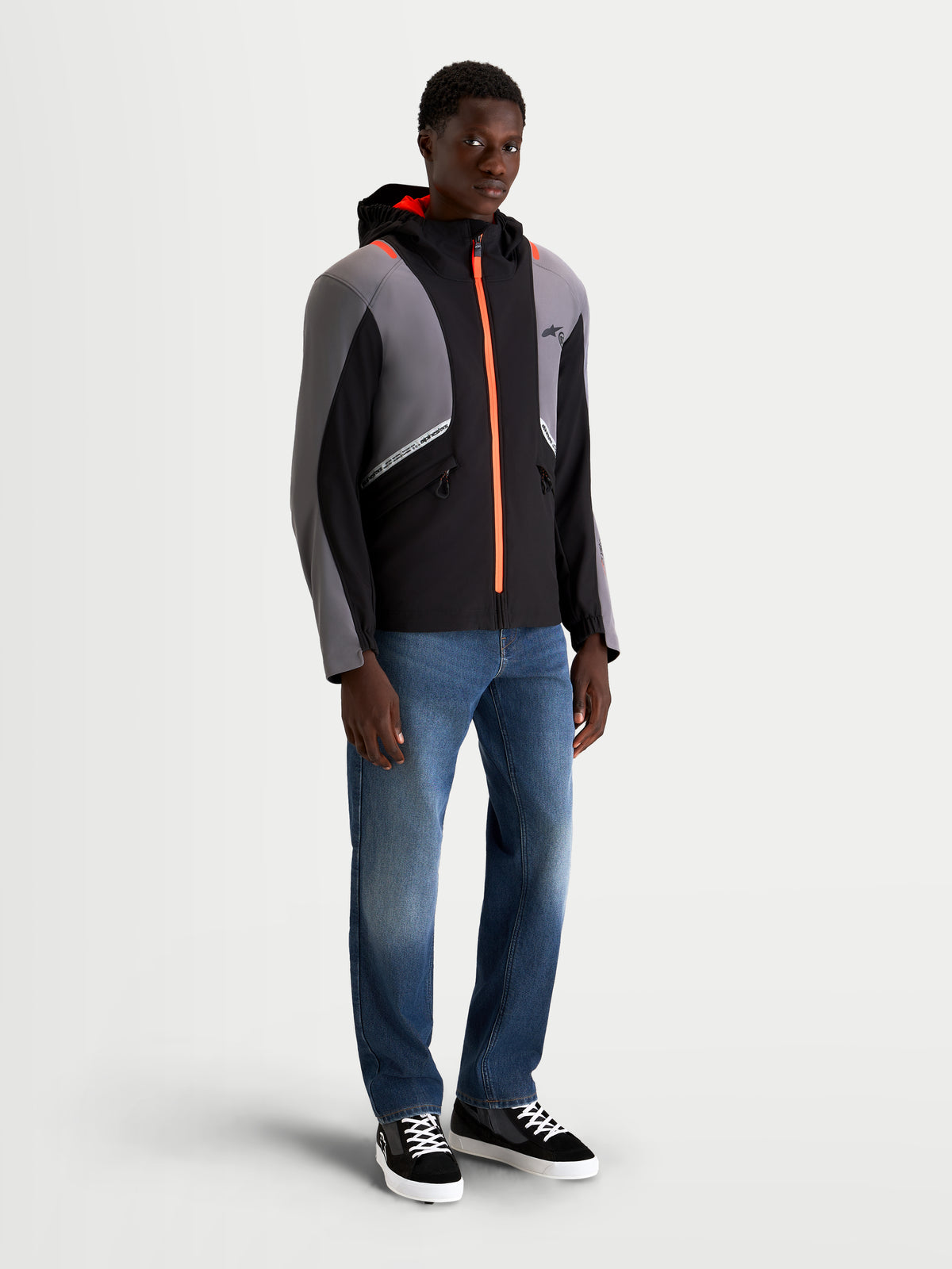 Alpinestars C 5 Drystar Giacca, giacca da moto urbana contemporanea da uomo in nero e grigio scuro, con cappuccio integrato, struttura impermeabile e dettagli con zip arancioni accesi indossata da un modello