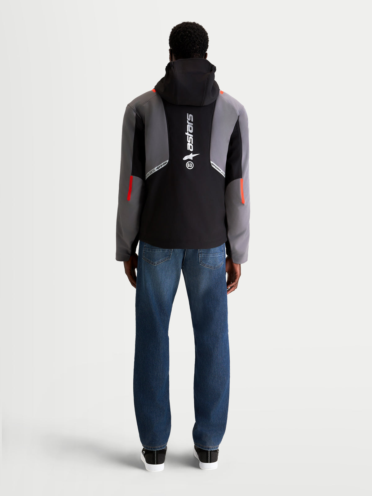 Alpinestars C 5 Drystar Giacca, giacca da moto urban contemporanea da uomo in nero e grigio scuro, vista posteriore su un modello che indossa jeans, con cappuccio integrato e grande logo verticale sulla schiena