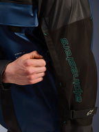 Giacca Alpinestars Mospher WP in Nero Dark Petrol, dettaglio della manica con branding Alpinestars color petrolio, una mano che regola la cerniera di ventilazione, tessuto ripstop resistente e cinturino regolabile sul braccio