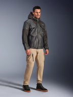 Modello che indossa la giacca Alpinestars Mospher Waterproof in nero, parka impermeabile d'ispirazione utility con design multitasche e cappuccio, abbinato a pantaloni cargo color sabbia e sneaker alte nere, abbigliamento moto urban per pendolari.