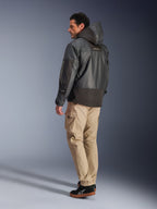Uomo che indossa la giacca impermeabile Alpinestars Mospher WP in nero, vista posteriore e di profilo laterale, abbinata a pantaloni cargo color sabbia e sneakers nere. Design parka con cappuccio in tessuto ripstop, marchio Alpinestars sulla manica e stile urban moderno per motociclisti.