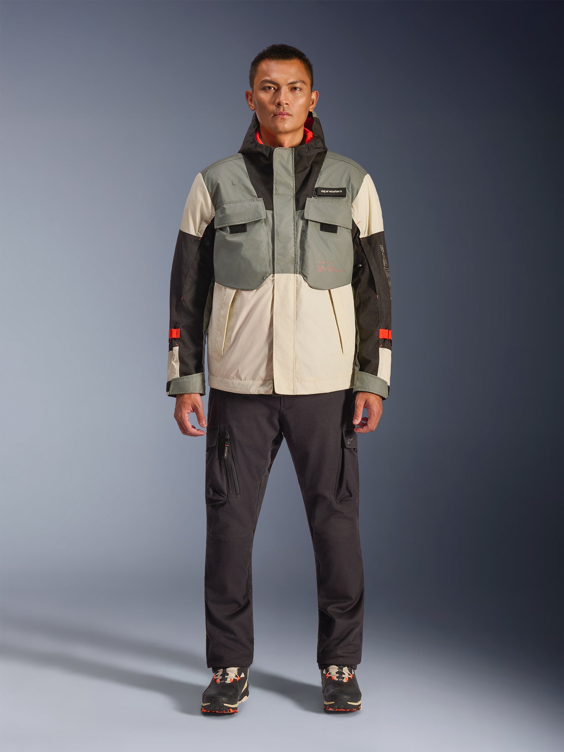 Giacca Alpinestars Mospher Waterproof in Fur Gray Black Ice, parka da moto in stile tattico indossato da un modello con pantaloni cargo scuri, design multitasche con pannelli a blocchi di colore grigio, crema e nero, abbigliamento da moto per pendolari urbani