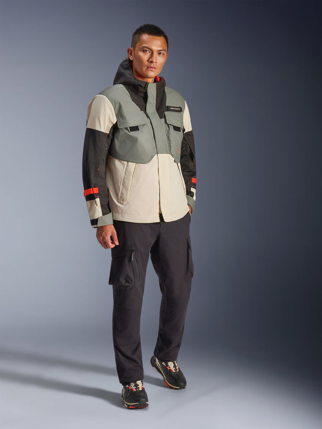 Giacca Alpinestars Mospher Waterproof in Fur Gray Black Ice, parka tecnico da moto multicolore con pannelli grigi, neri e bianco sporco e accenti rossi, design funzionale con ampie tasche e cappuccio, indossata con pantaloni cargo grigio scuro e sneakers nere, abbigliamento da moto urban contemporary