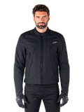 Giacca Alpinestars Clayton WR, giacca da moto nera, indossata da un modello, con dettagli trapuntati sulle spalle e grafiche tecniche, cerniera Vislon centrale, tasche verticali con zip, piccolo logo bianco sul petto, abbigliamento da guida urbana per uso stradale