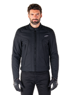Giacca Alpinestars Clayton WR, giacca da moto nera, indossata da un modello, con dettagli trapuntati sulle spalle e grafiche tecniche, cerniera Vislon centrale, tasche verticali con zip, piccolo logo bianco sul petto, abbigliamento da guida urbana per uso stradale