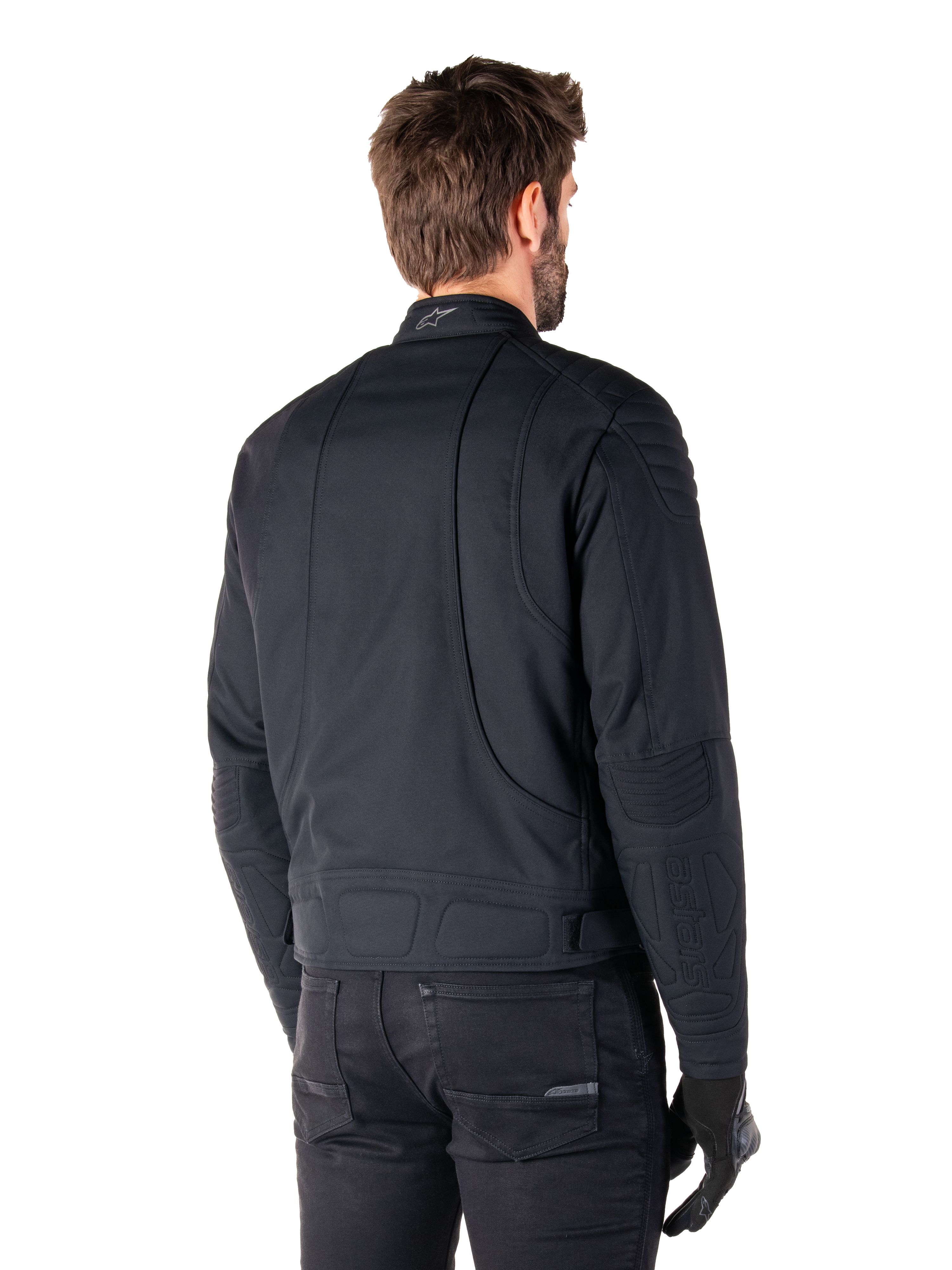 Giacca Alpinestars Clayton WR in nero, vista posteriore di tre quarti su un modello maschile, giacca da moto urbana con imbottitura trapuntata su spalle e gomiti, linee di cucitura tecniche e logo riflettente sul colletto, abbinata a pantaloni e guanti neri.